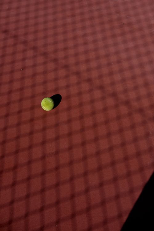 Free Tennis ball on a clay court with net shadow creates a striking sports composition. Stock Photo