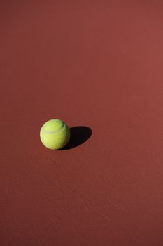A single tennis ball casting a shadow on a sunlit clay court, emphasizing simplicity.