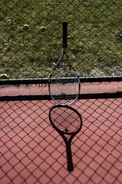 A Tennis Racket Leaning on a Wire Mesh Fence
