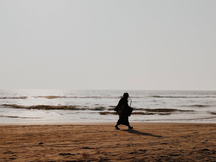 A Silhouette Of A Person Walking On A Beach