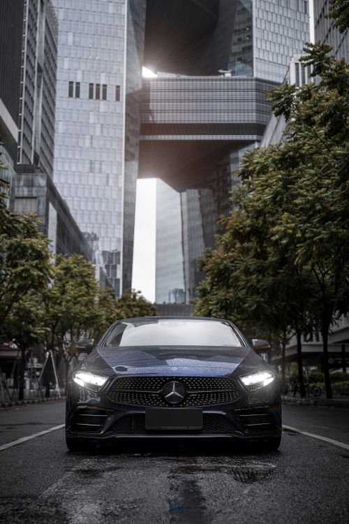 Free A black Mercedes Benz AMG GT on a wet urban street, flanked by towering skyscrapers. Stock Photo