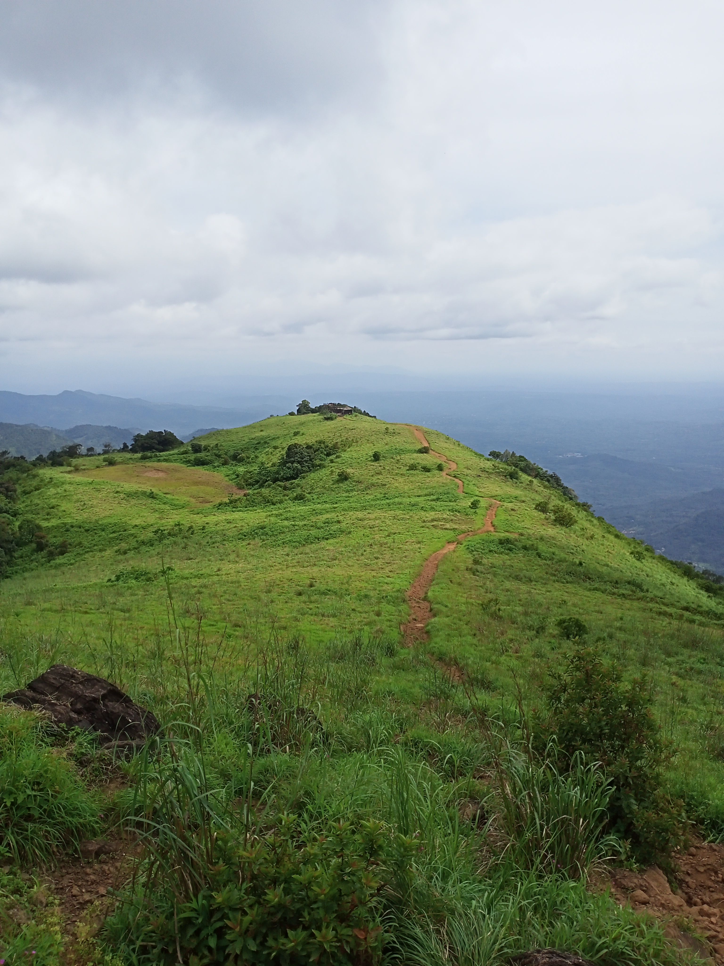 A scenic view of a green mountain trail leading into lush nature under a cloudy sky.