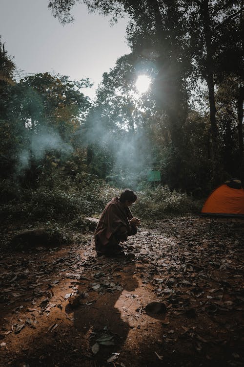 Woman Crouching near a Tent in a Forest