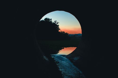 Free A tranquil view through a tunnel at sunset, capturing reflections on a calm body of water. Stock Photo