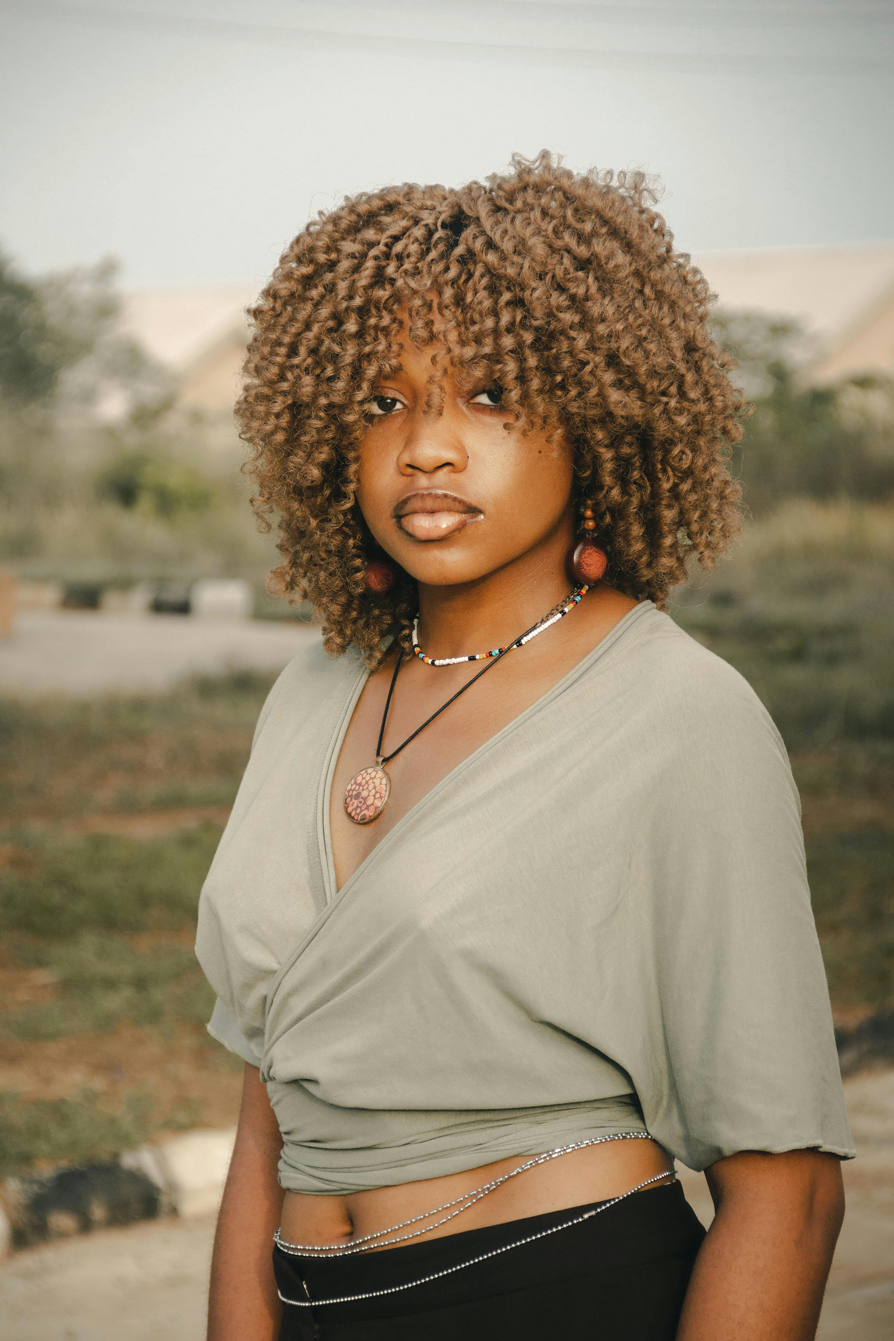 Portrait of a young woman with curly hair in an outdoor setting looking confidently at the camera.