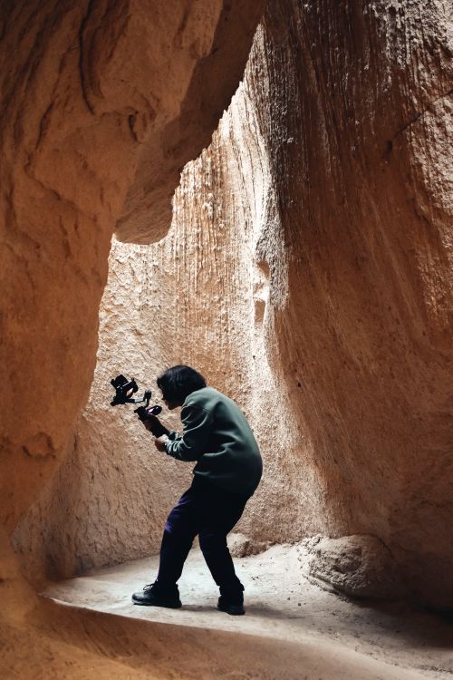 Free A photographer capturing shots inside a naturally lit rocky cave passage. Stock Photo