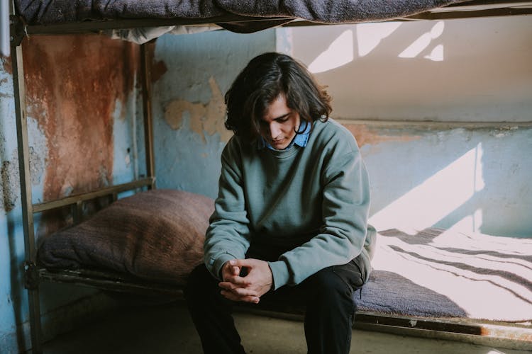 Man In A Green Sweatshirt Sitting On A Bed