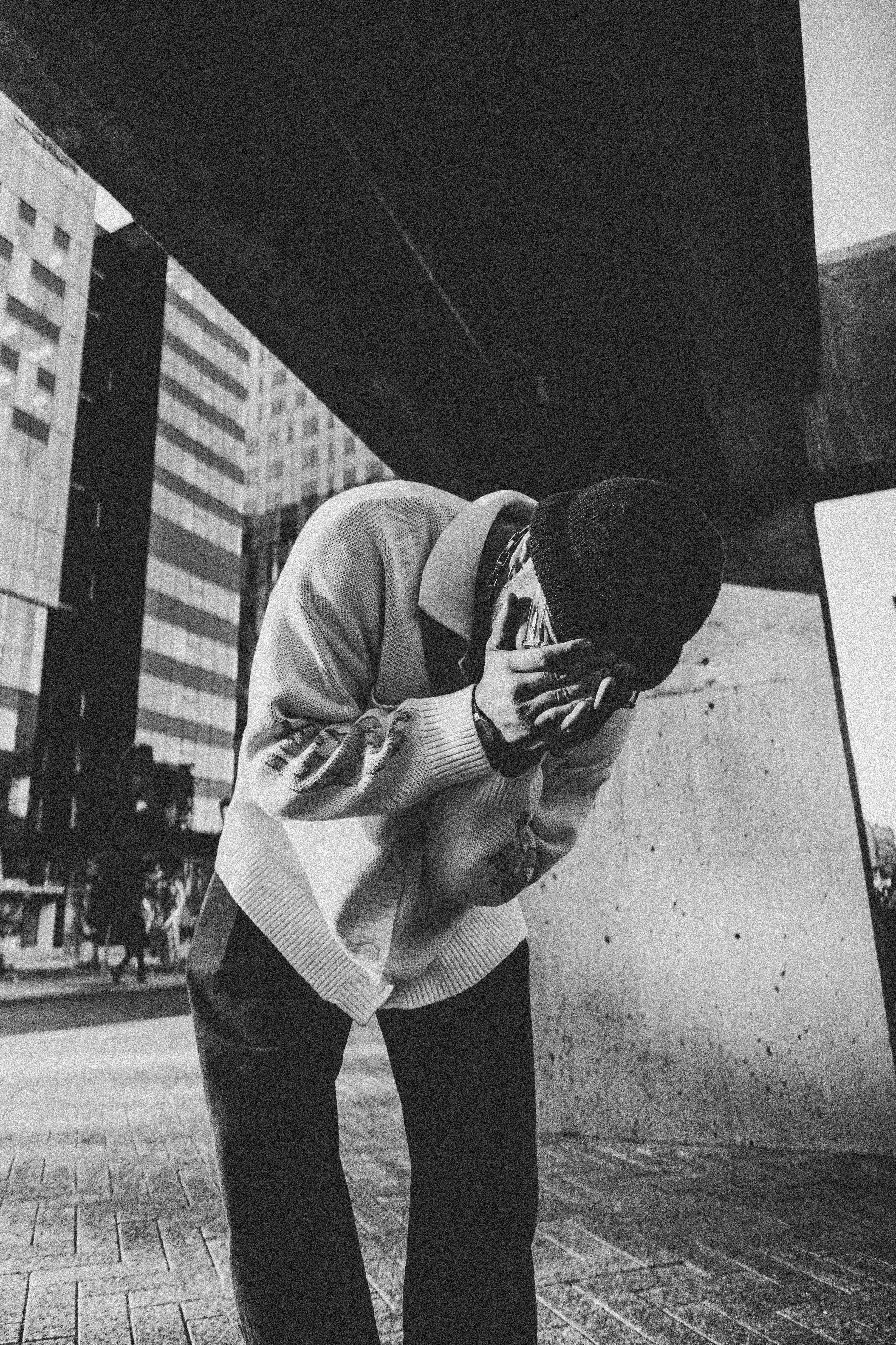 A contemplative person stands in a modern city street scene, captured in black and white.