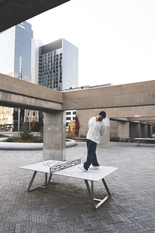 Free A man in white long sleeves stands on a graffiti-covered table in an urban setting. Stock Photo