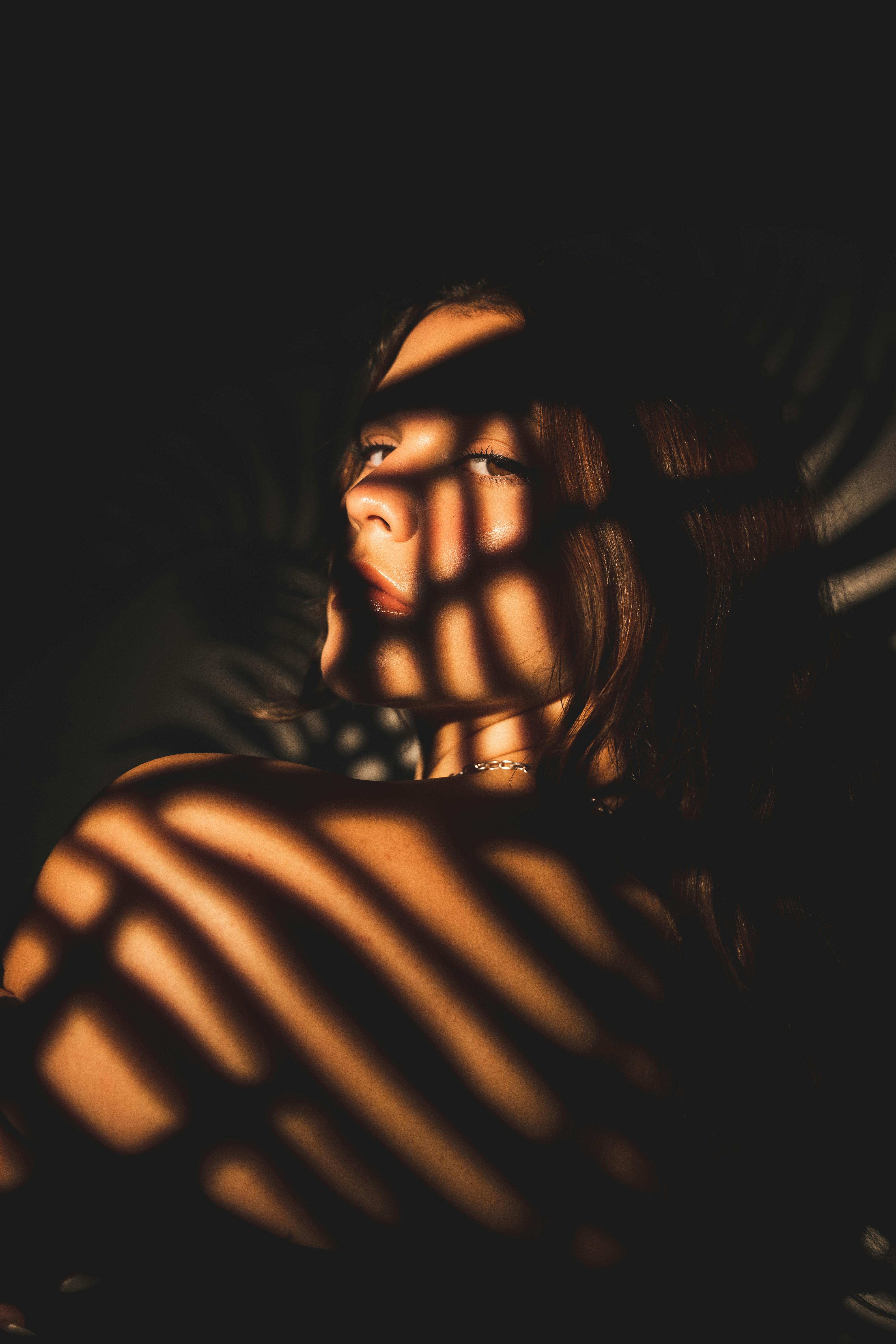 An artistic portrait of a young woman with dramatic palm leaf shadows on her face.