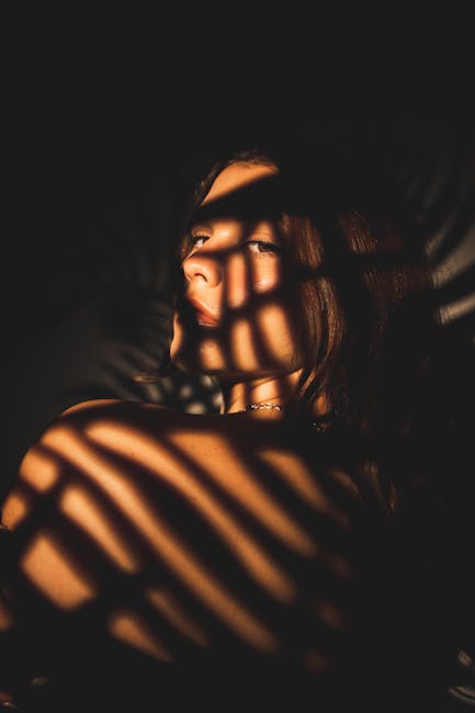 An artistic portrait of a young woman with dramatic palm leaf shadows on her face.