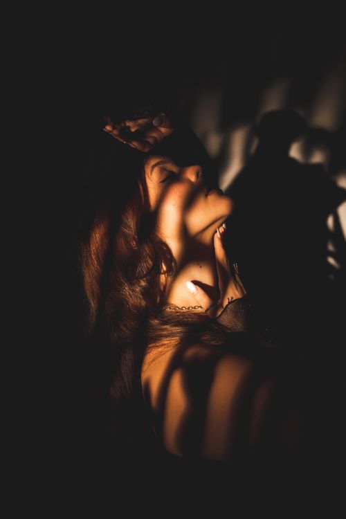 Free A dramatic portrait of a woman with eyes closed, featuring artistic shadows and sunlight interplay. Stock Photo