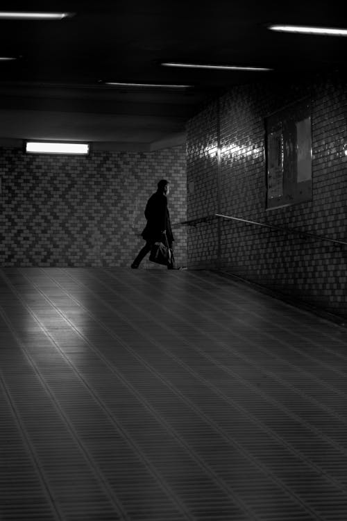 Grayscale Photo of Man Walking on Hallway 