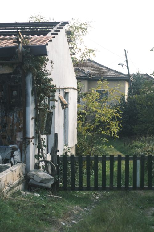 Free Weathered house with a rustic wooden fence amidst lush greenery, evoking a serene countryside ambiance. Stock Photo