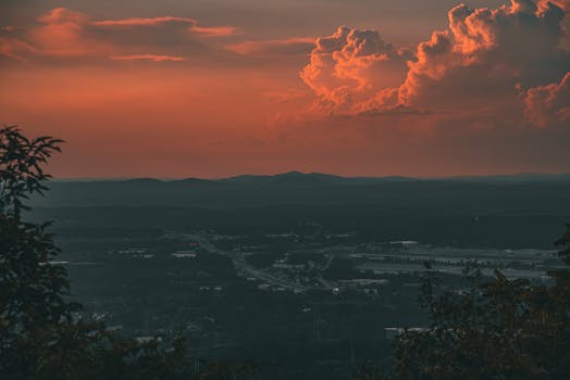 Dramatic sunset with vivid orange clouds over a silhouetted landscape and distant hills.