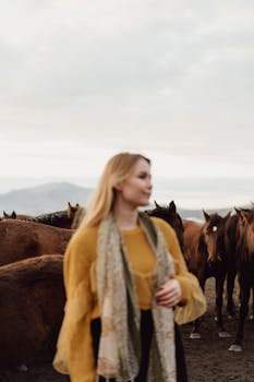 A woman in a pasture, surrounded by horses, creating a serene and natural scene.
