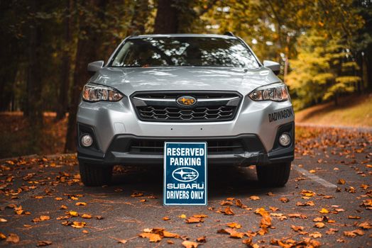 Front view of a silver Subaru Crosstrek parked outdoors with a reserved parking sign for Subaru drivers during fall.