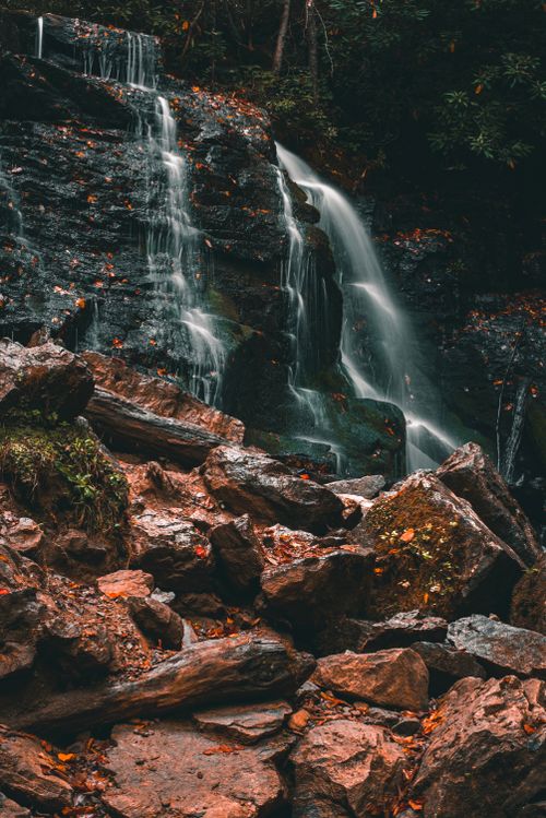 Free Capture the serene beauty of a cascading waterfall surrounded by autumn forest scenery and rocks. Stock Photo