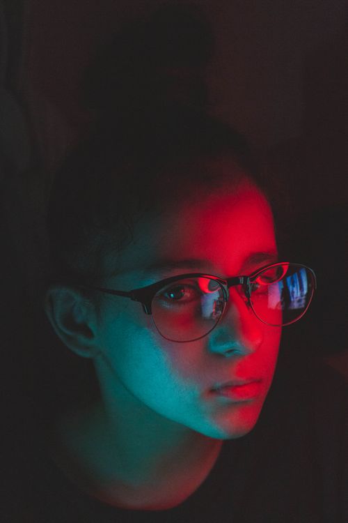 Free Close-up portrait of a girl wearing eyeglasses with dramatic neon red and blue lighting. Stock Photo