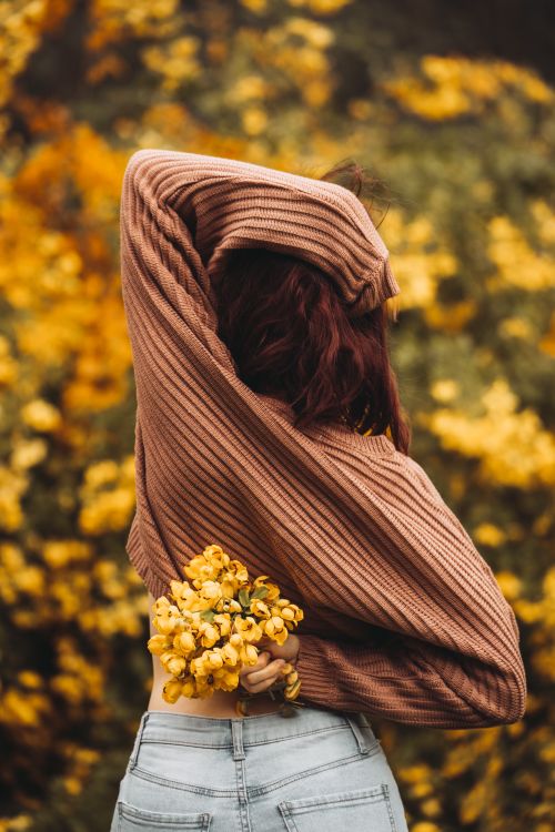 Free A woman in a sweater and jeans holds a bouquet of yellow flowers in a blooming garden. Stock Photo