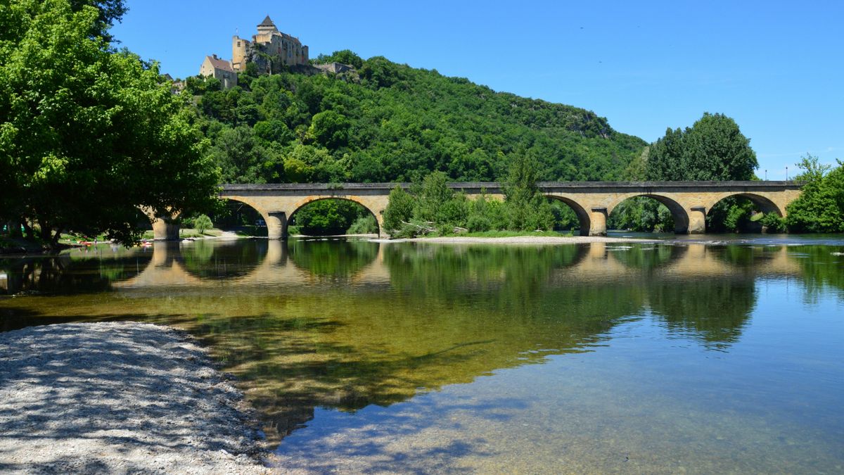 Château de Castelnaud above the honey-stone bridge reflected in the Dordogne