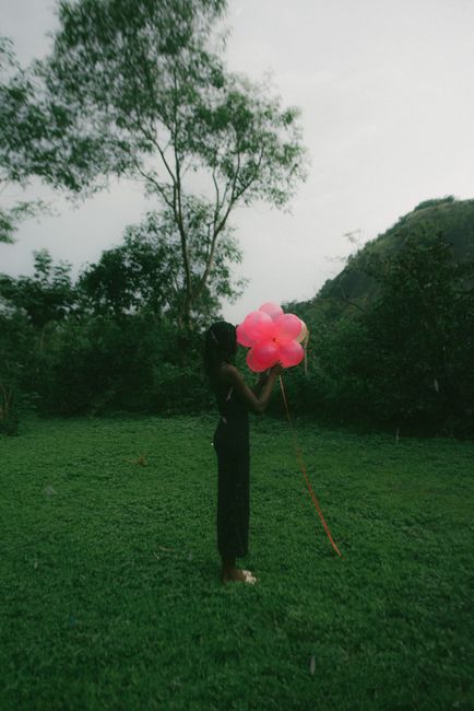A woman in a meadow holding a vibrant flower-shaped balloon, evoking a sense of serenity.