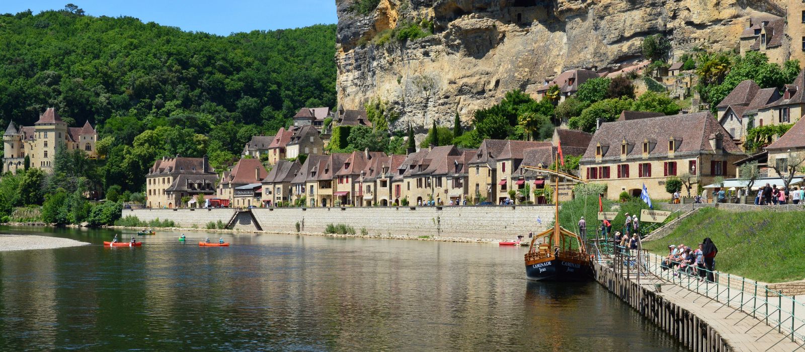 Picturesque riverside village in Dordogne, France with historic buildings and lush greenery.