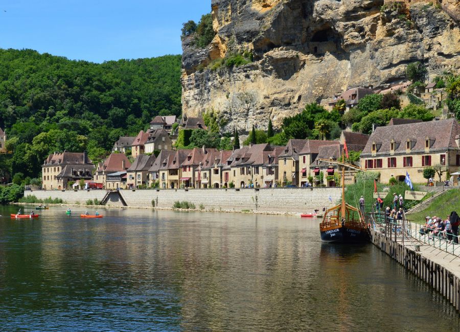 Picturesque riverside village in Dordogne, France with historic buildings and lush greenery.