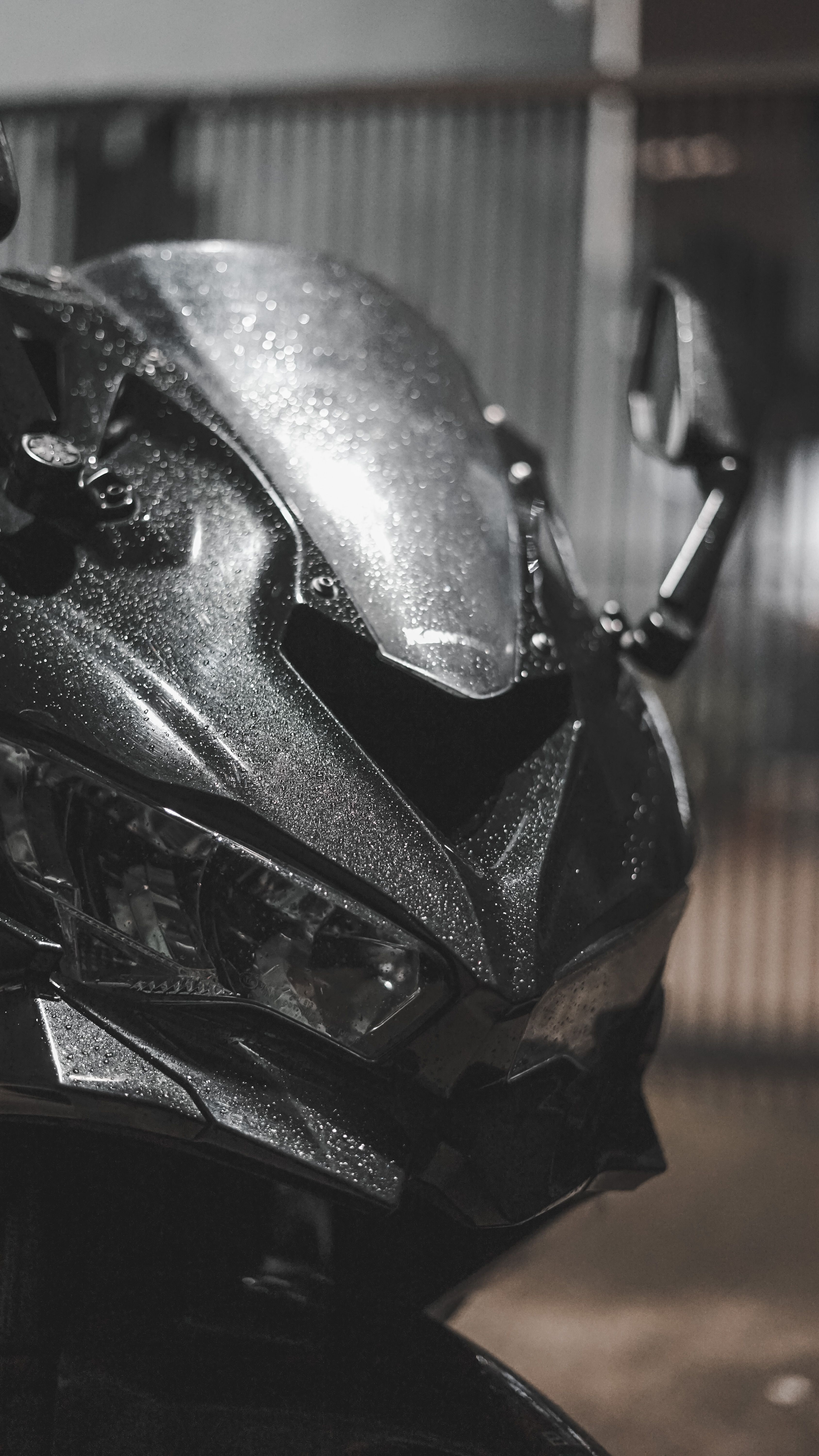 Detailed close-up of a motorcycle's front with raindrops, showcasing sleek design under low light.