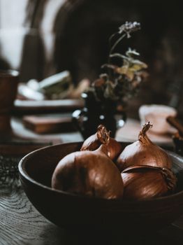 Warm still life of onions in a wooden bowl on a rustic kitchen table.