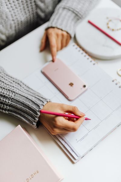 Person planning a schedule on a phone next to a notebook