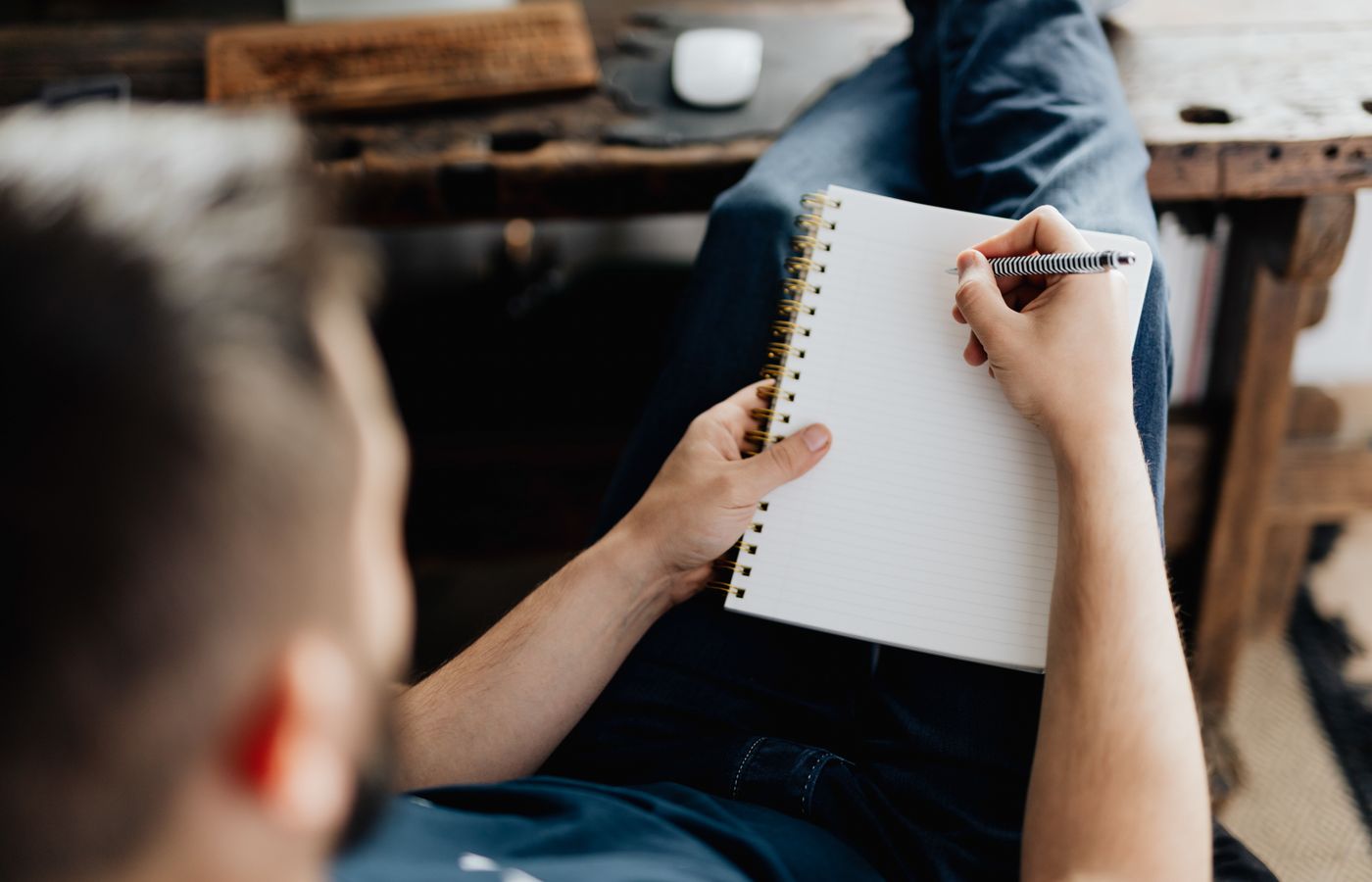 Man lying back and writing on a notebook, relaxing at home. Cozy setting with a rustic desk.