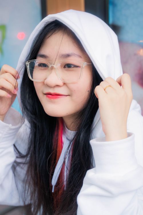 Free Joyful teen with glasses and long dark hair in a white hoodie, smiling warmly. Stock Photo