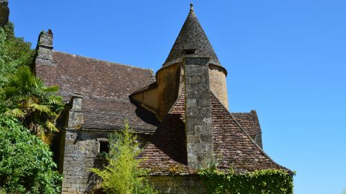 Free An ancient stone house with a unique rooftop and lush plants under a clear summer sky. Stock Photo