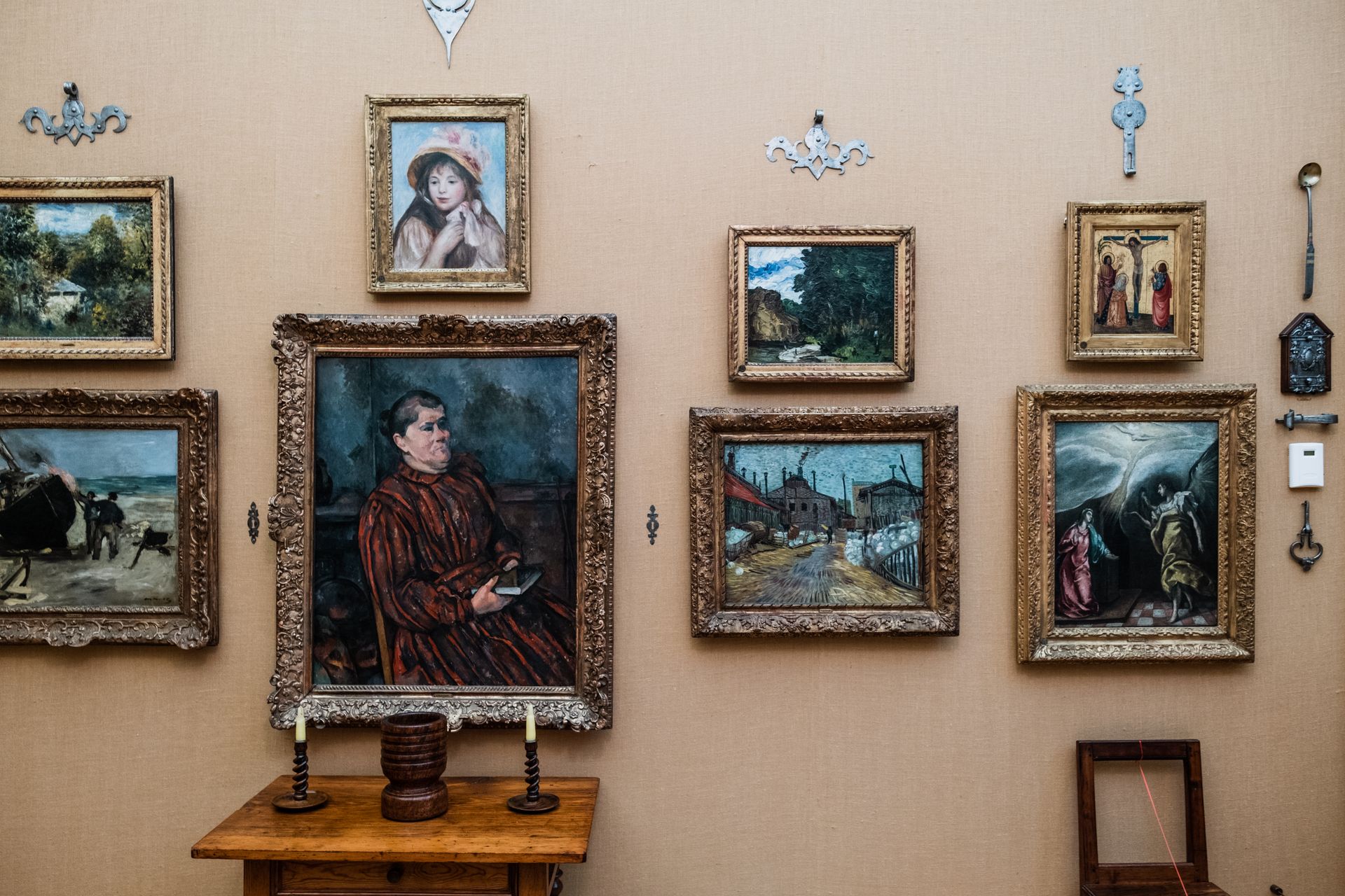 A gallery wall featuring a variety of framed paintings set against a beige background with decorative elements.