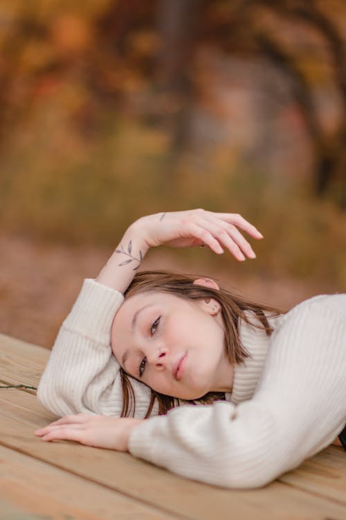 A Woman in White Turtleneck Sweater Lying Down on a Wooden Table