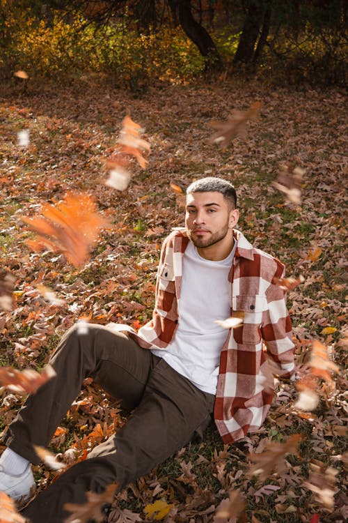 Man in Jacket and White T-Shirt Sitting on Fallen Leaves