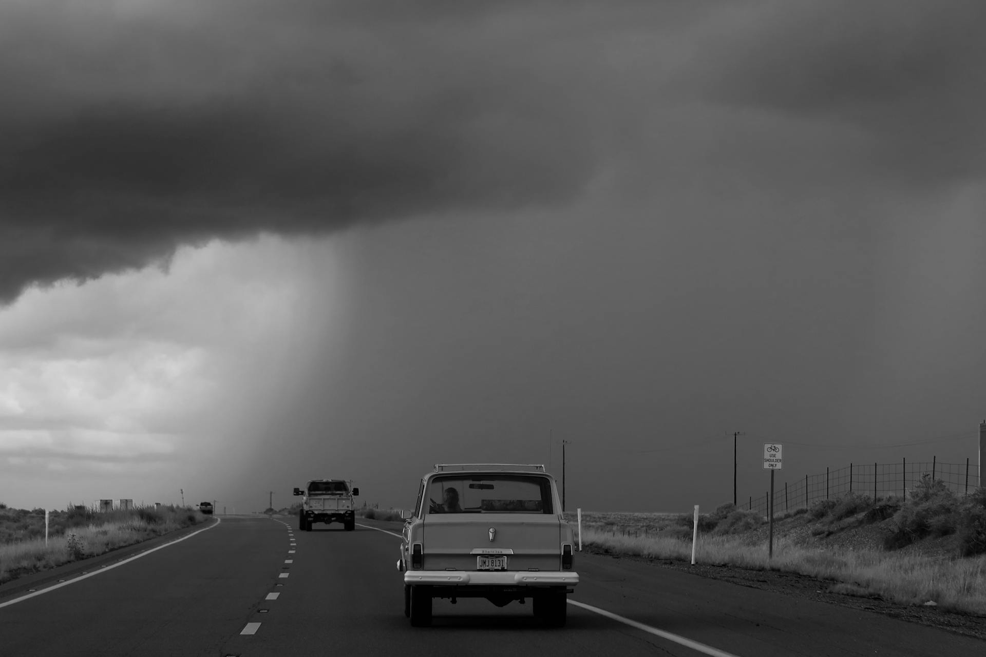 Monochrome scene of cars on an Oklahoma highway under a looming stormy sky.