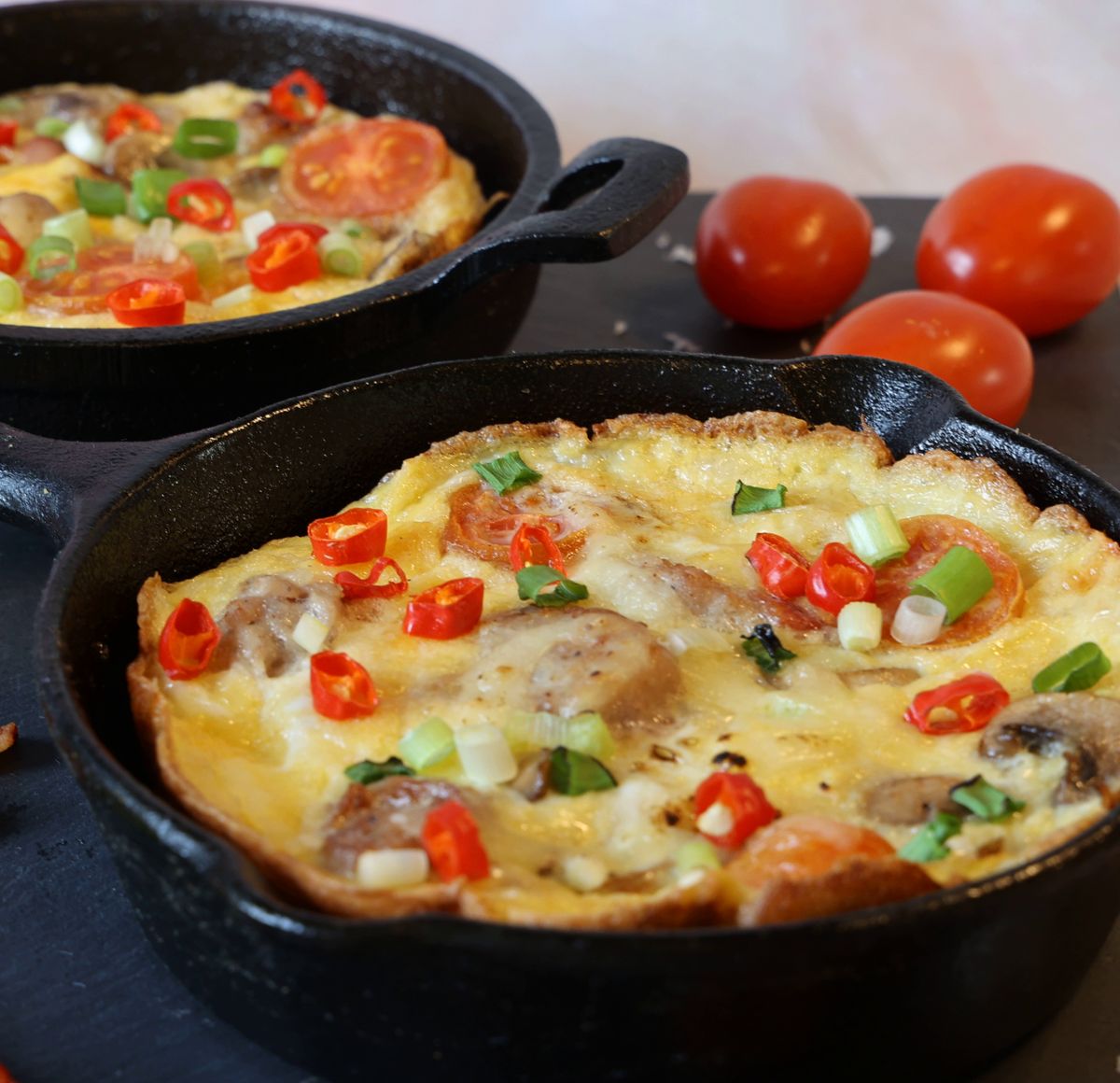 Cast iron skillet frittata with sausage, mushrooms, cherry tomatoes, red chilies and scallions