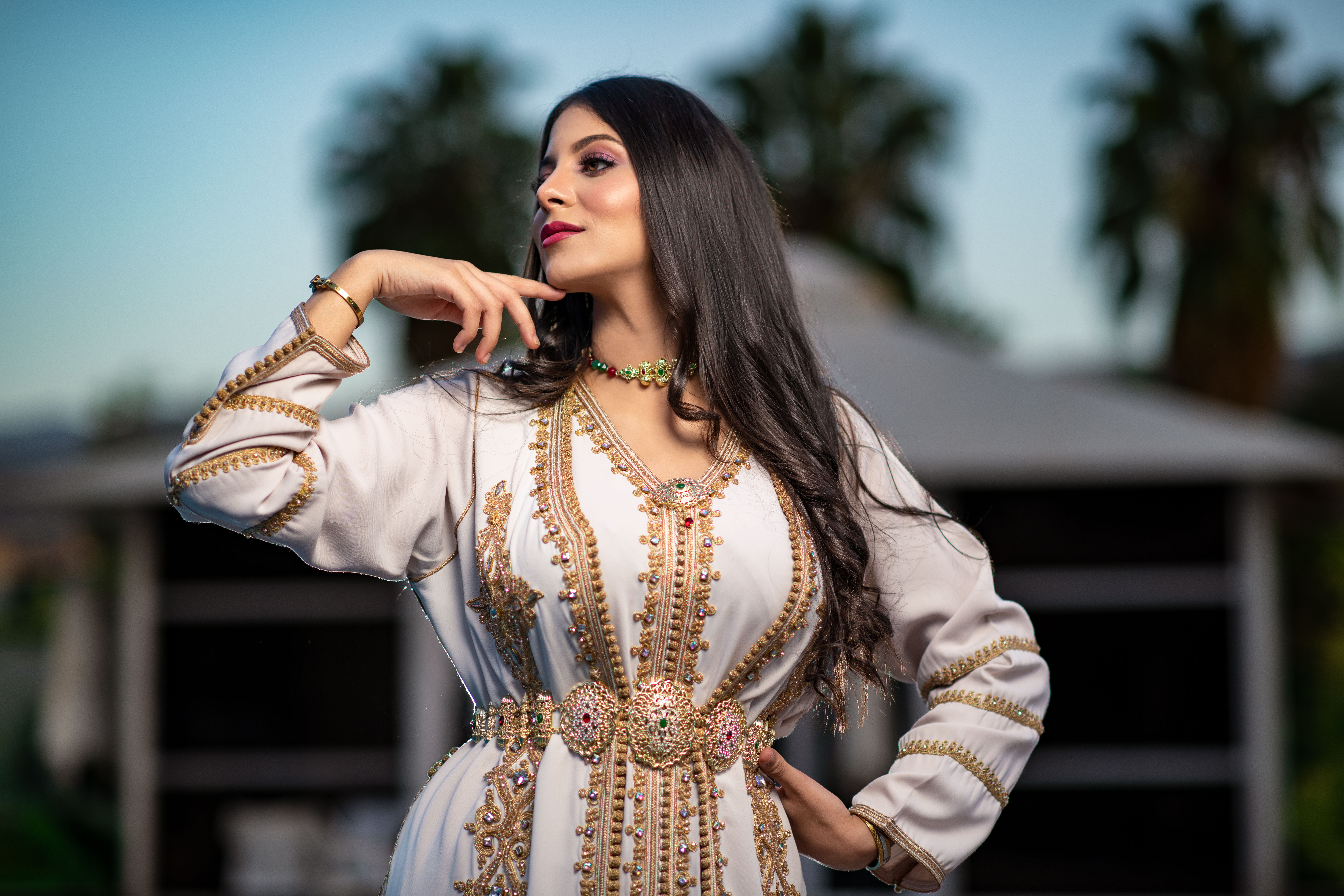 Elegant woman poses in an ornate dress against a blurred background outdoors in Ibiza, showcasing fashion and beauty.