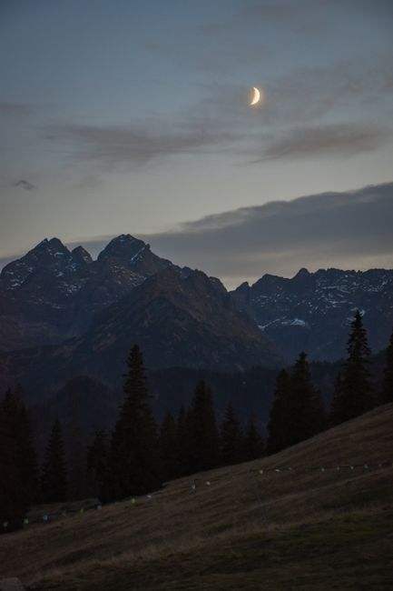 Scenic view of Tatra Mountains with a crescent moon at twilight, showcasing nature's tranquil beauty.