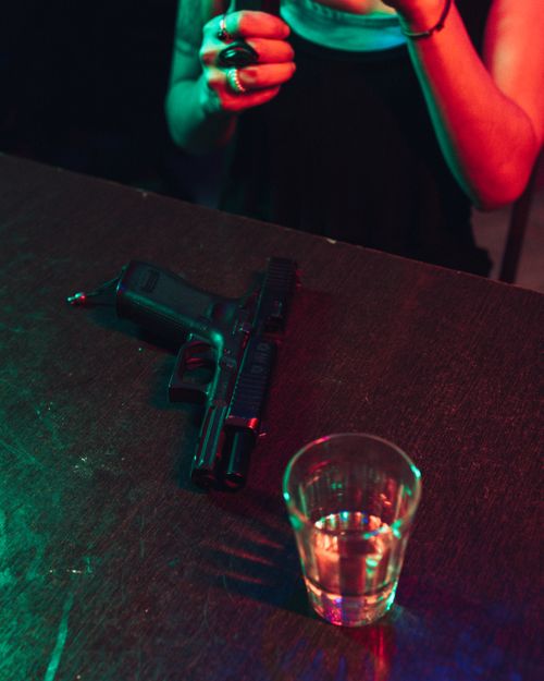 Free A dramatic indoor scene featuring a glass of whiskey and a handgun on a table, highlighting contrast and mood. Stock Photo