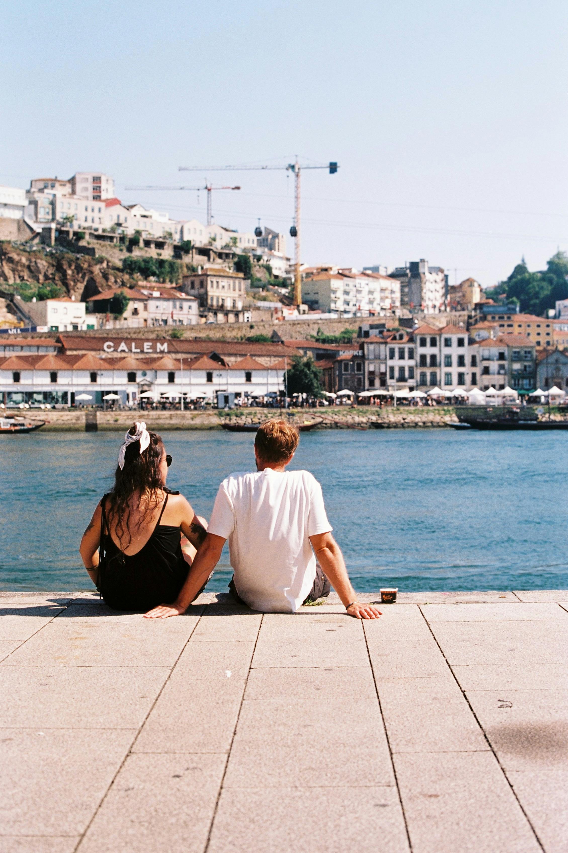 A couple relaxing by the river in Porto, Portugal, enjoying a sunny urban landscape.