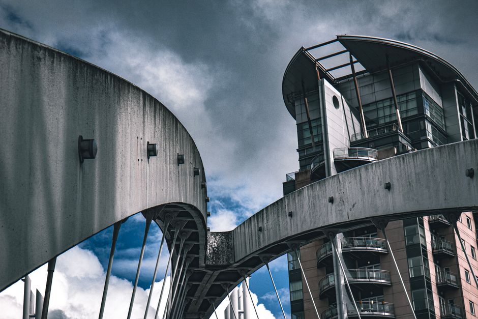 Dynamic shot of modern bridge and building facade under a cloudy sky in Salford, UK.