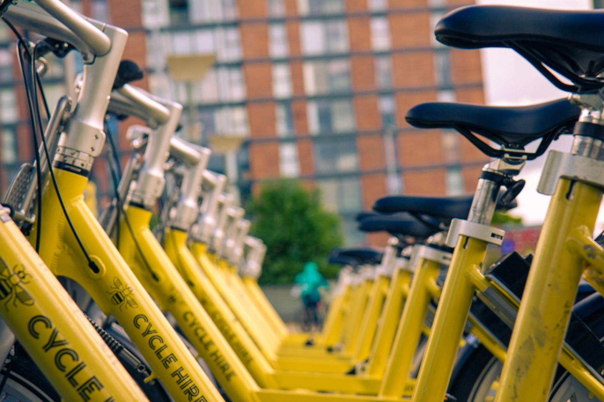 Row of yellow hire bicycles lined up outside urban building in Salford, UK.