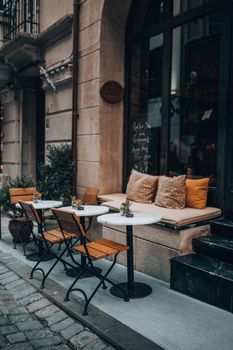 A cozy outdoor café with wooden chairs and marble tables along a cobblestone street, perfect for relaxation.