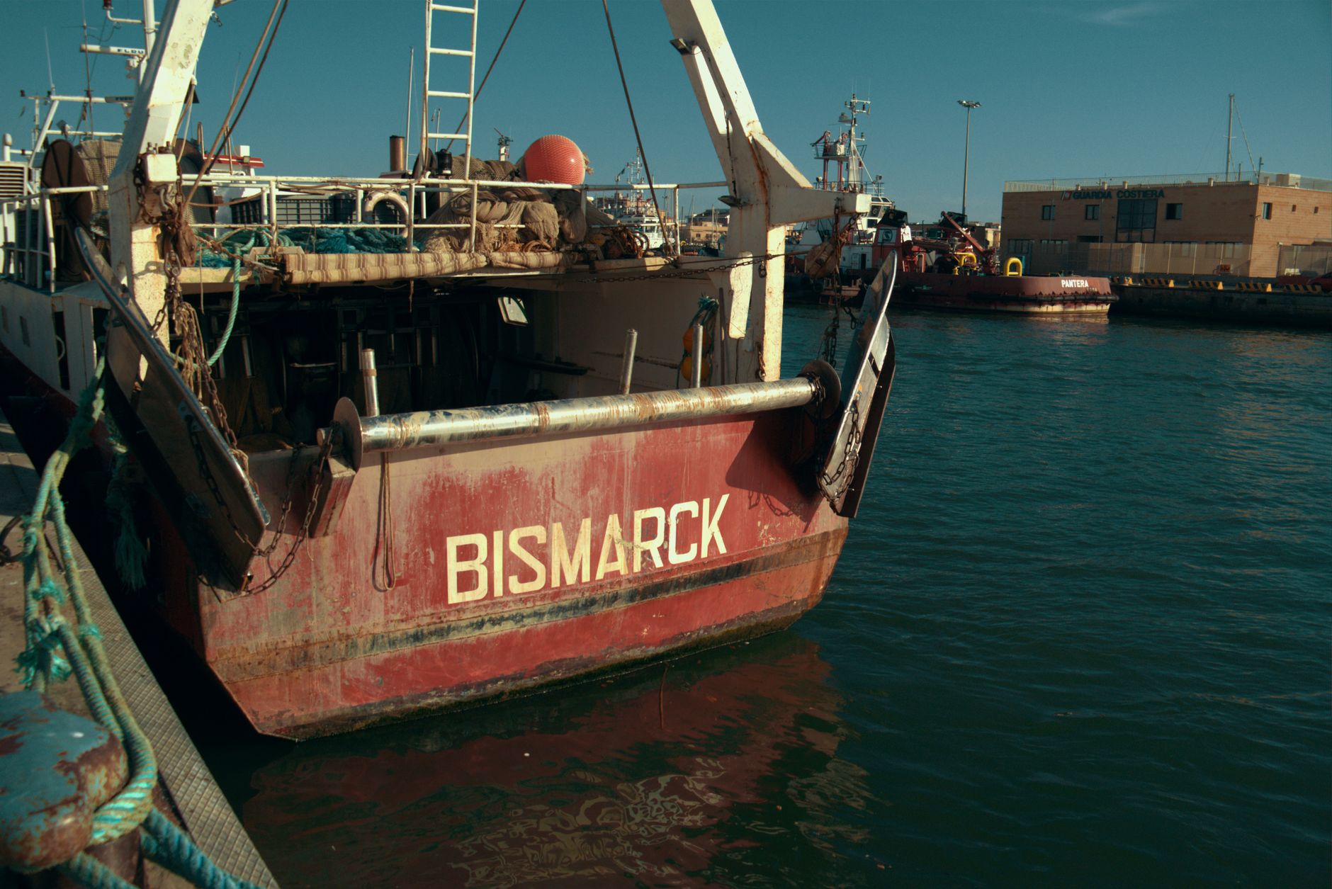 Back view of the Bismarck fishing vessel docked at an industrial harbor under clear skies.