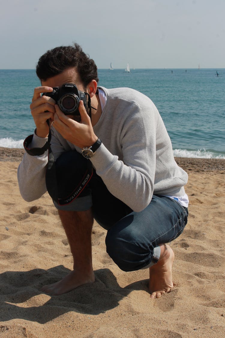 A Man In A Gray Sweater Taking A Picture With His Camera At A Beach