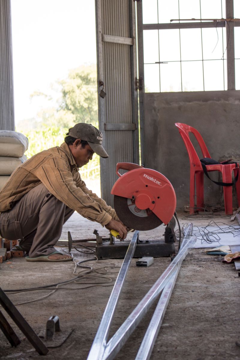 Man cuts metal with a cut-off saw in a sunlit workshop environment.