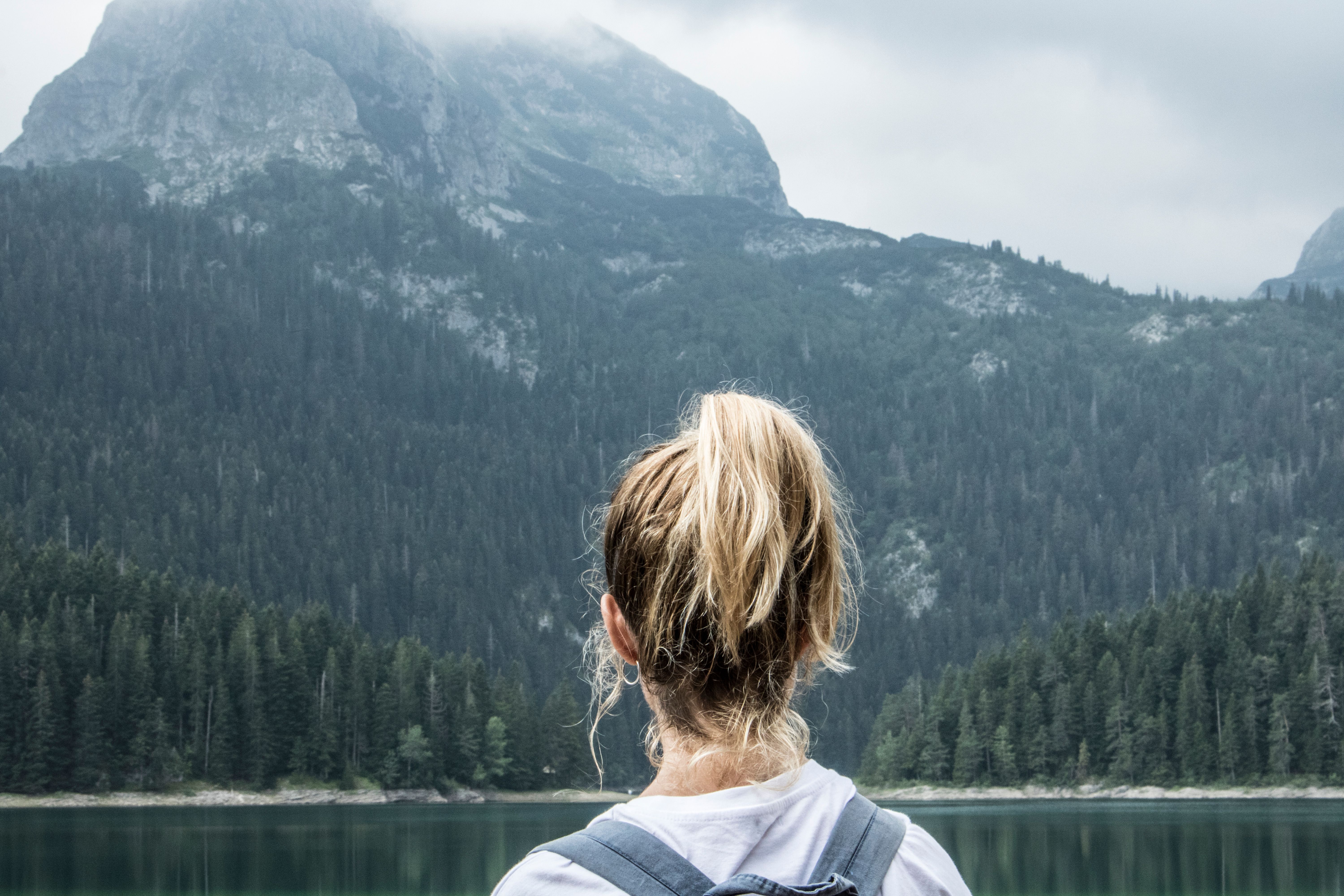 A woman with a backpack stands in front of a majestic mountainous landscape, embracing nature\'s tranquility.
